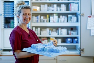 Eine Frau steht mit einem Tablett voller Medikamente vor einem Medikamentenschrank.