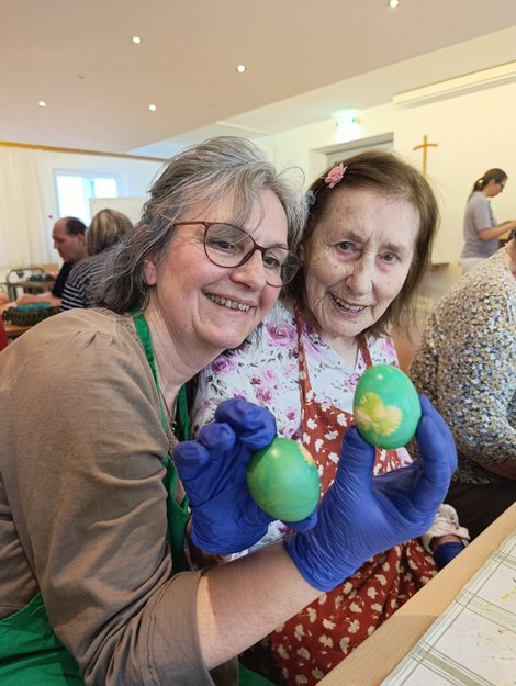 Ehrenamtliche Mitarbeiterin Christl mit Bewohnerin und grün gefärbten Ostereiern