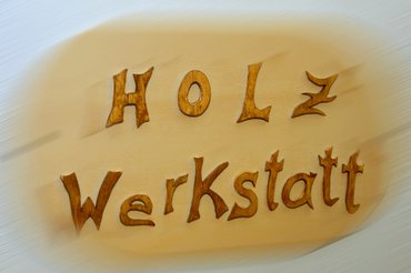 Ein Schild mit der Aufschrift "Holzwerkstatt". Die Buchstaben sind aus Holz geschnitzt.