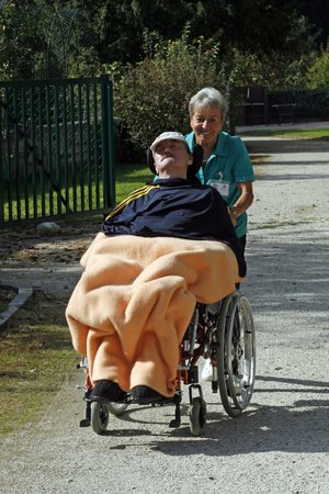 freiwillige Mitarbeiterin geht mit einem Bewohner im Rollstuhl spazieren