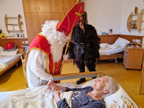 Nikolaus und Krampus im Zimmer bei bettlägeriger Bewohnerin.