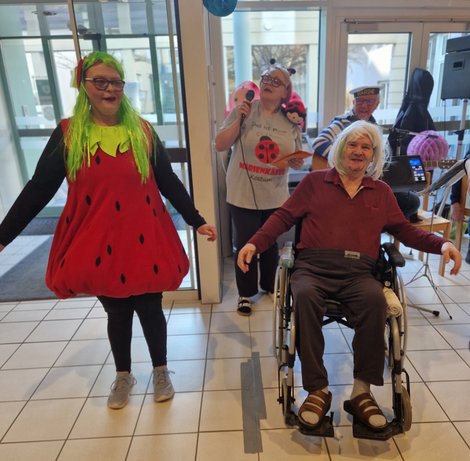 Mitarbeiterin in Erdbeer-Kostüm und Bewohner im Rollstuhl beim Faschingsfest