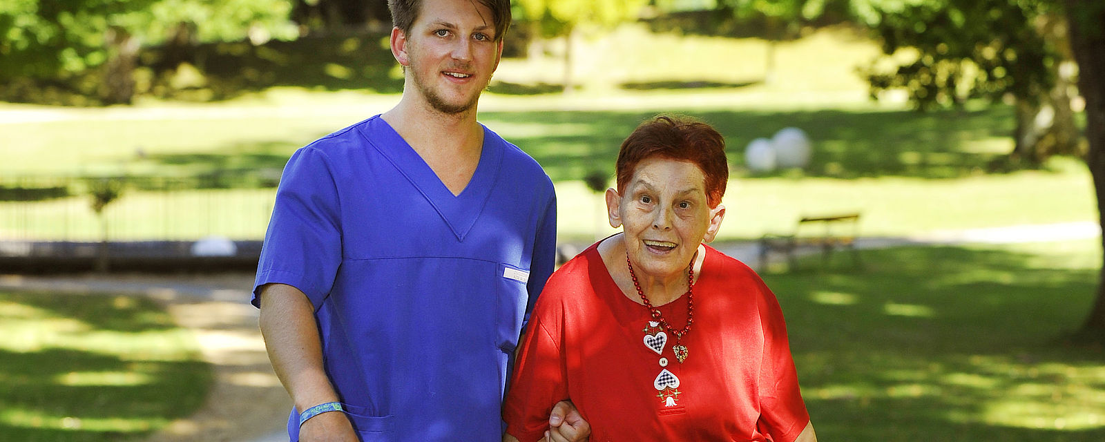 Mitarbeiter und Bewohnerin gehen durch die Grünanlage des Schlosses