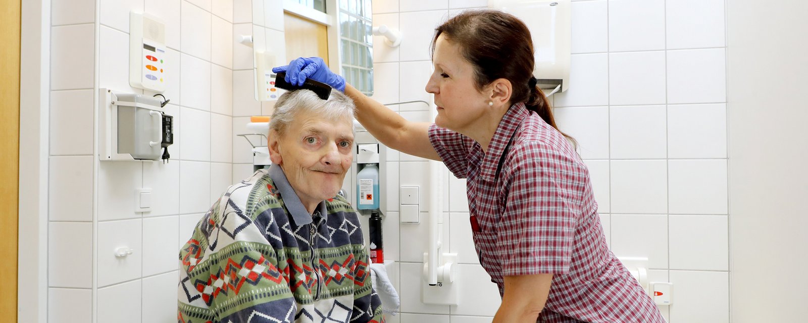 Mitarbeiterin kämmt einem Bewohner die Haare