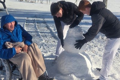 Bewohner im Rollstuhl und 2 Zivildiener beim Bauen eines Schneemanns