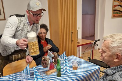 Mitarbeiter mit Maiskrug; 2 BewohnerInnen rätseln