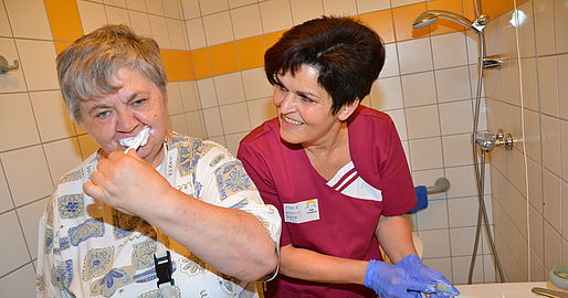 Mitarbeiterin sieht einer Bewohnerin beim Zähneputzen zu