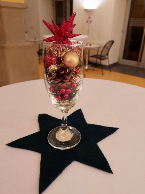 Tischdeko: weihnachtlich gefülltes Sektglas in rot-gold auf schwarzem Filzstern