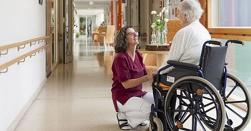 Mitarbeiterin im Gespräch mit einer Bewohnerin im Rollstuhl