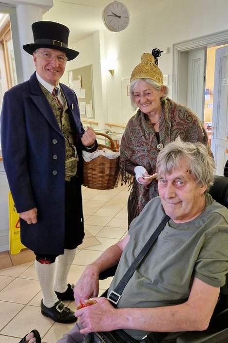 Bewohner im Rollstuhl freut sich über Lebkuchenherz von Mitglied des Gmundner Trachtenvereins