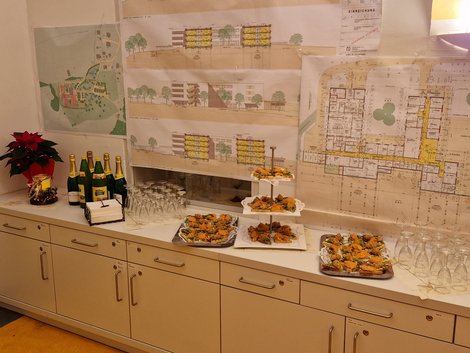 Buffet im Vordergrund, Hauspläne an der Wand