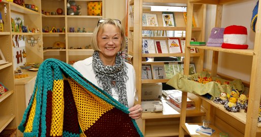 Mitarbeiterin mit gehäkelter Decke in der Hand im Verkaufsraum