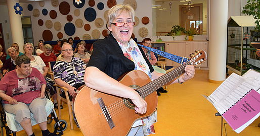 Mitarbeiterin mit Gitarre singt mit den Bewohnerinnen und Bewohnern