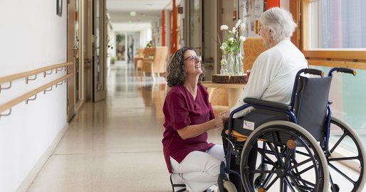 Mitarbeiterin im Gespräch mit einer Bewohnerin im Rollstuhl