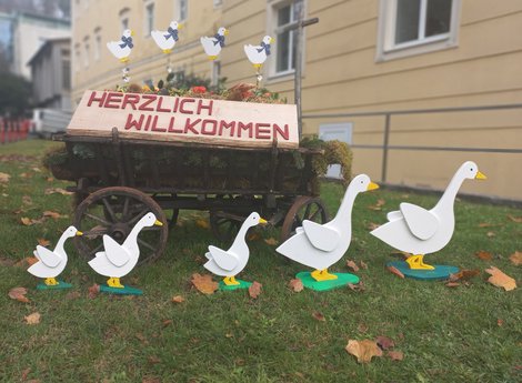 Heuwagen mit Schild: Herzlich Willkommen, davor Aufsteller in Form von Gänsen
