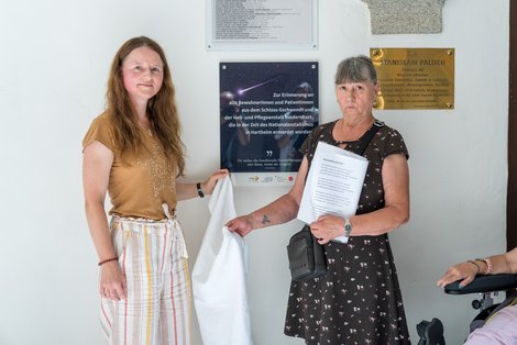 LPBZ-Geschäftsführerin Mag.a(FH) Christina Schwarzberger enthüllt mit LPBZ Schloss Gschwendt-Bewohnerin Gerlinde Zoitl die Gedenktafel zur Erinnerung an die in der NS-Zeit in Hartheim umgekommenen BewohnerInnen.